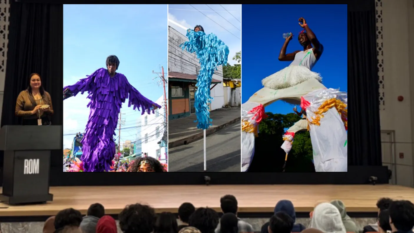A presenter on a stage in front of an audience stands behind a podium labelled ROM. The screen next to them displays a composite image of three dark-skinned people wearing colourful fringed outfits and walking on stilts.