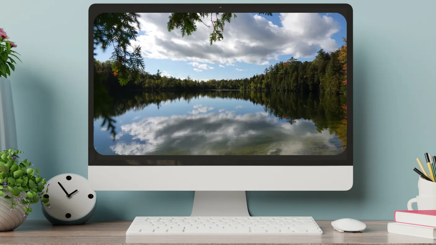 A computer screen on a desk displays an image of a glassy lake ringed by trees