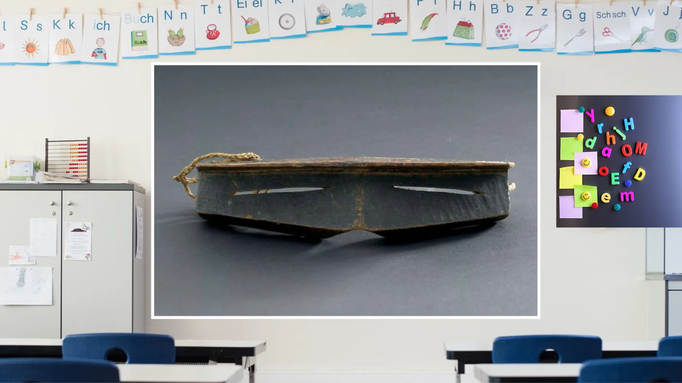 A colourful classroom with a display screen at the front. The screen shows iggaak (snow goggles) carved from wood with narrow horizontal slits for the eyes, and a string at the back.