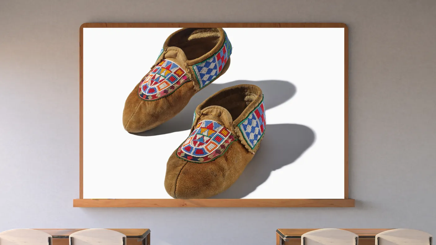 A screen in a classroom displays a pair of hide moccasins with colorful beading.