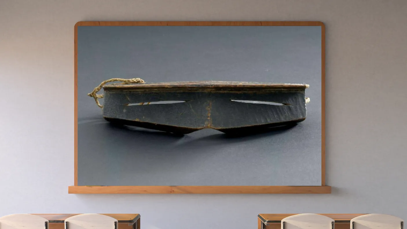 A classroom with a display screen at the front. The screen shows iggaak (snow goggles) carved from wood with narrow horizontal slits for the eyes, and a string at the back.