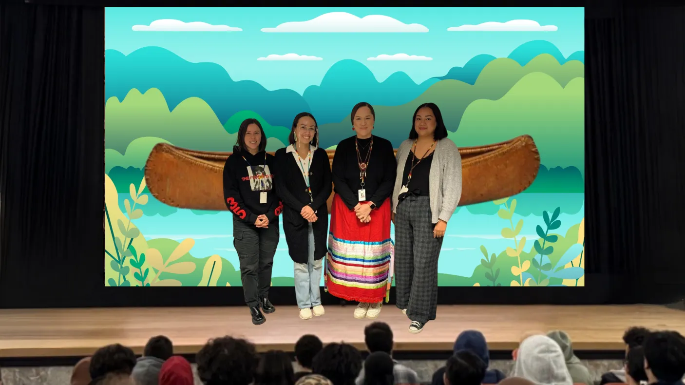 Four Indigenous women stand on a stage. The screen behind them displays an image of a canoe on an illustrated river.