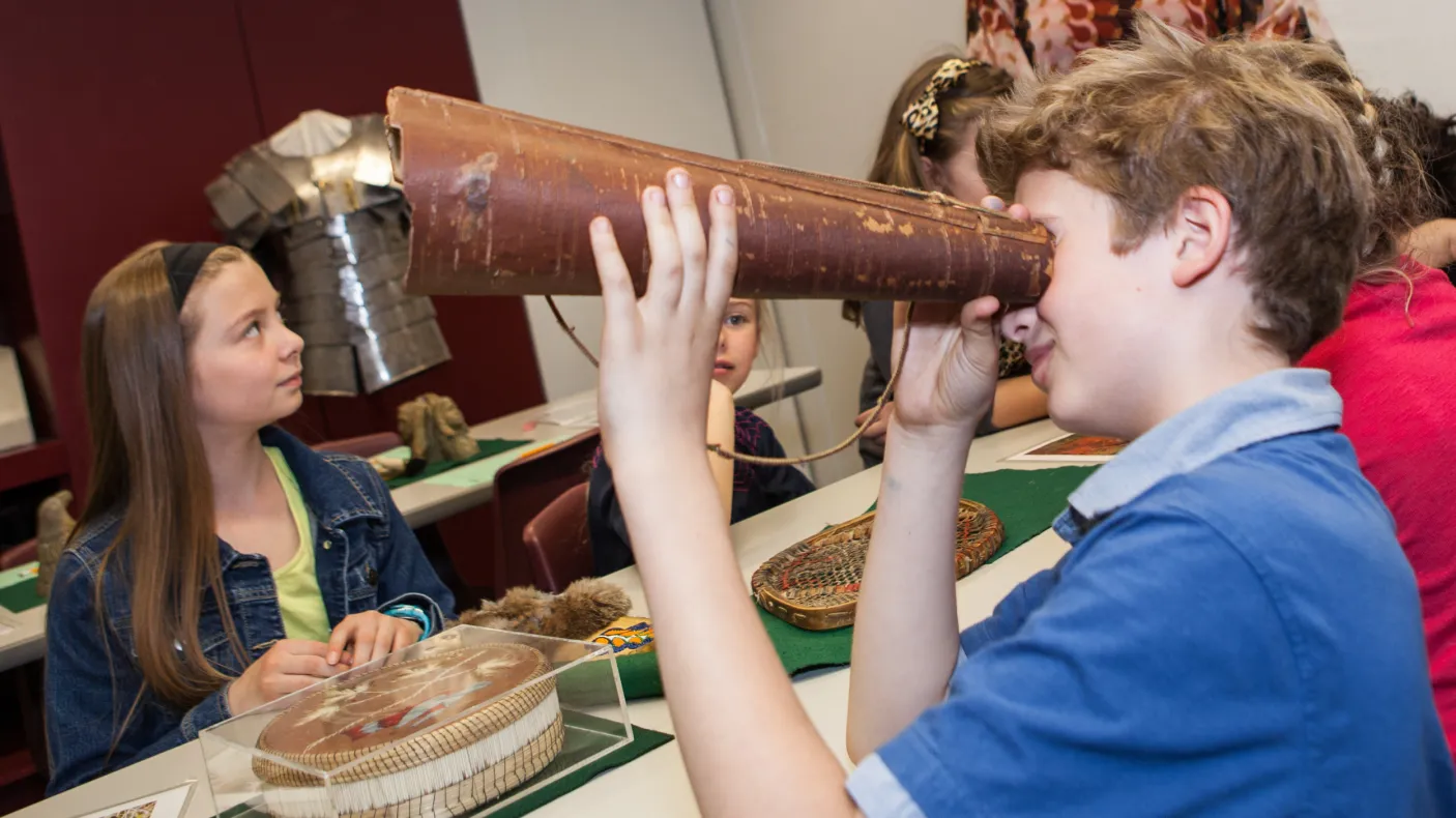 A student holds a birch bark moose call up to his eye while attempting to discern what it is.
