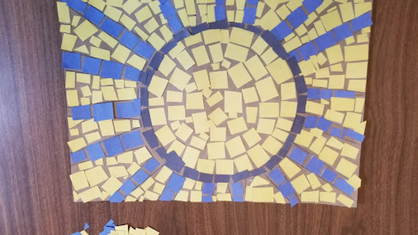 Mosaïque d'un soleil composée de carrés jaunes, bleus et noirs.
