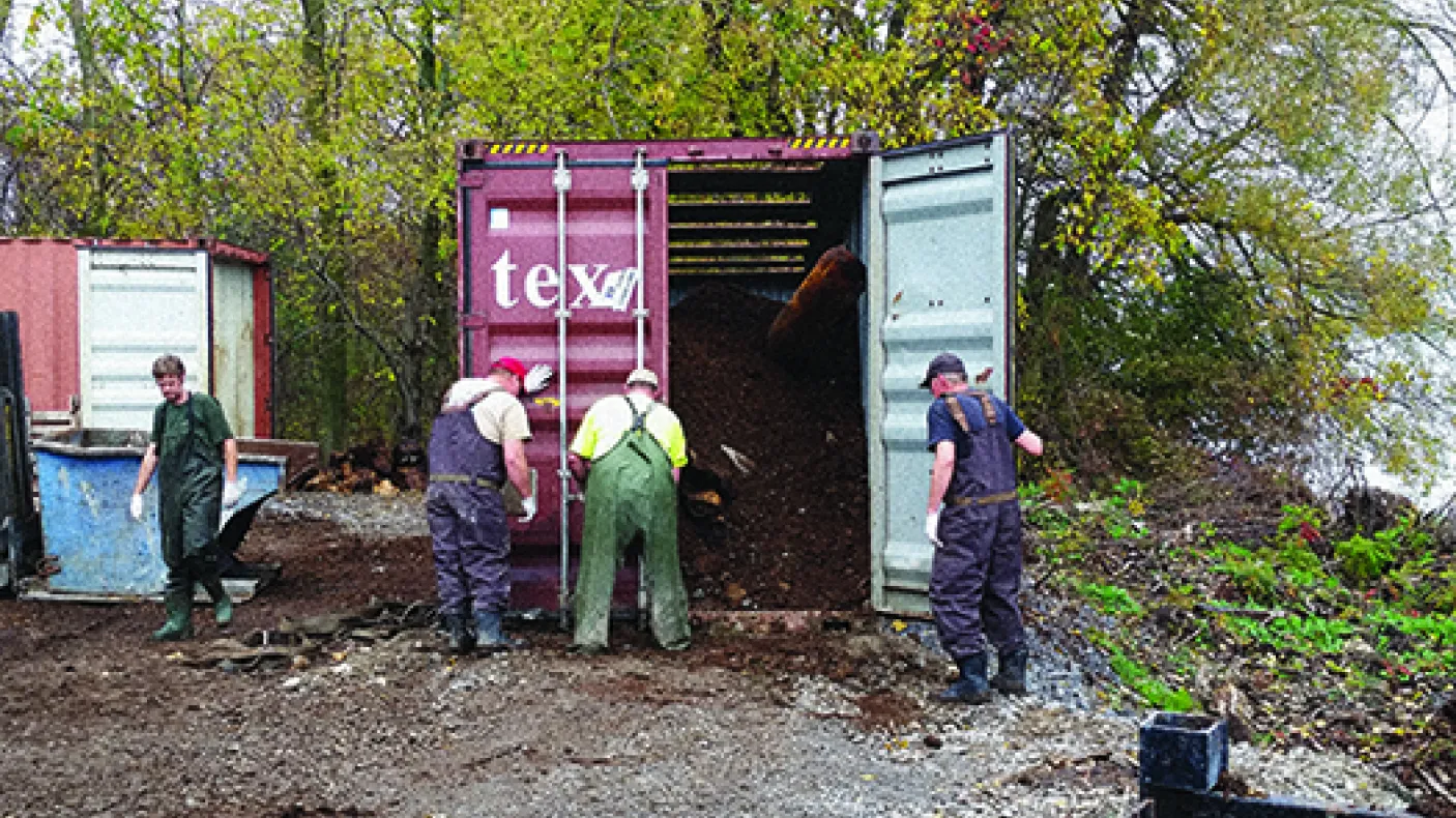 Three men working next to a shipping container that contains the Blue Whale bones and manure.
