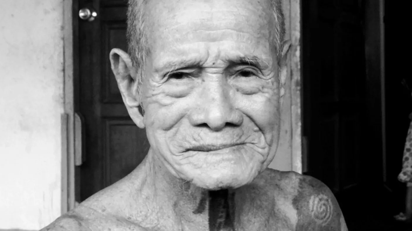 Black and white photograph of an older man with tattoos on his neck and shoulders
