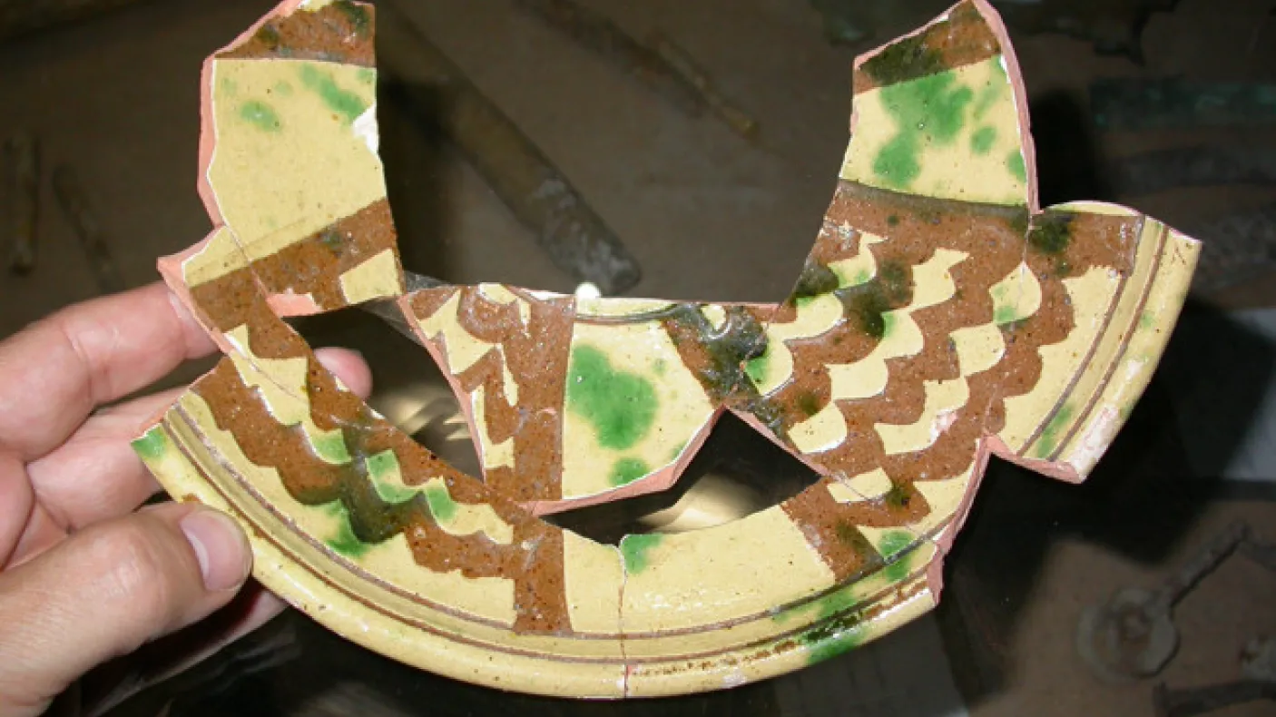 Pottery with an earthenware fired-clay body, overall white slip, incision through the slip with a broad tool, overall lead glaze, splashed with copper-green, probably mid-14th century.
