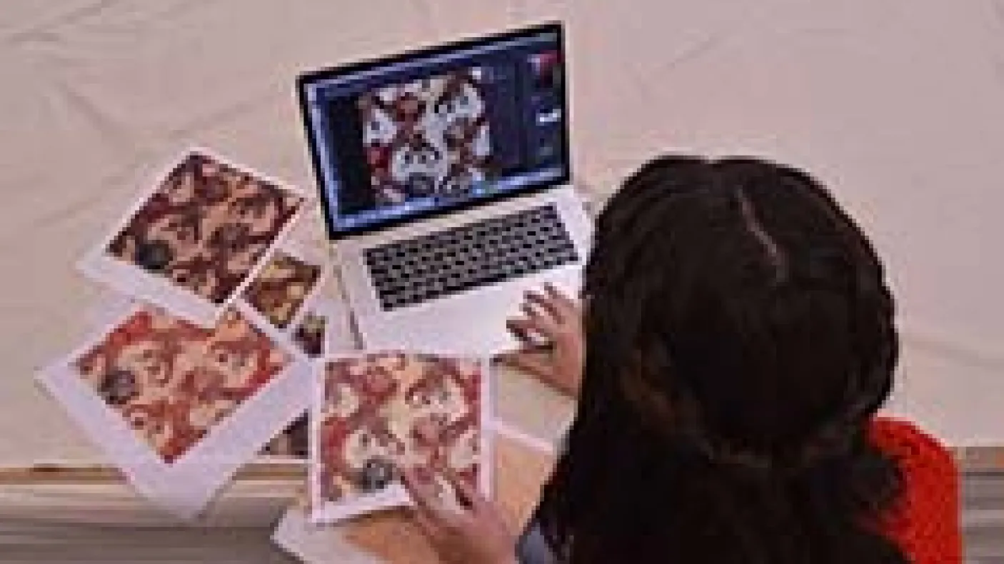 A young woman sits in front of a laptop computer surrounded by squares of patterned fabric.
