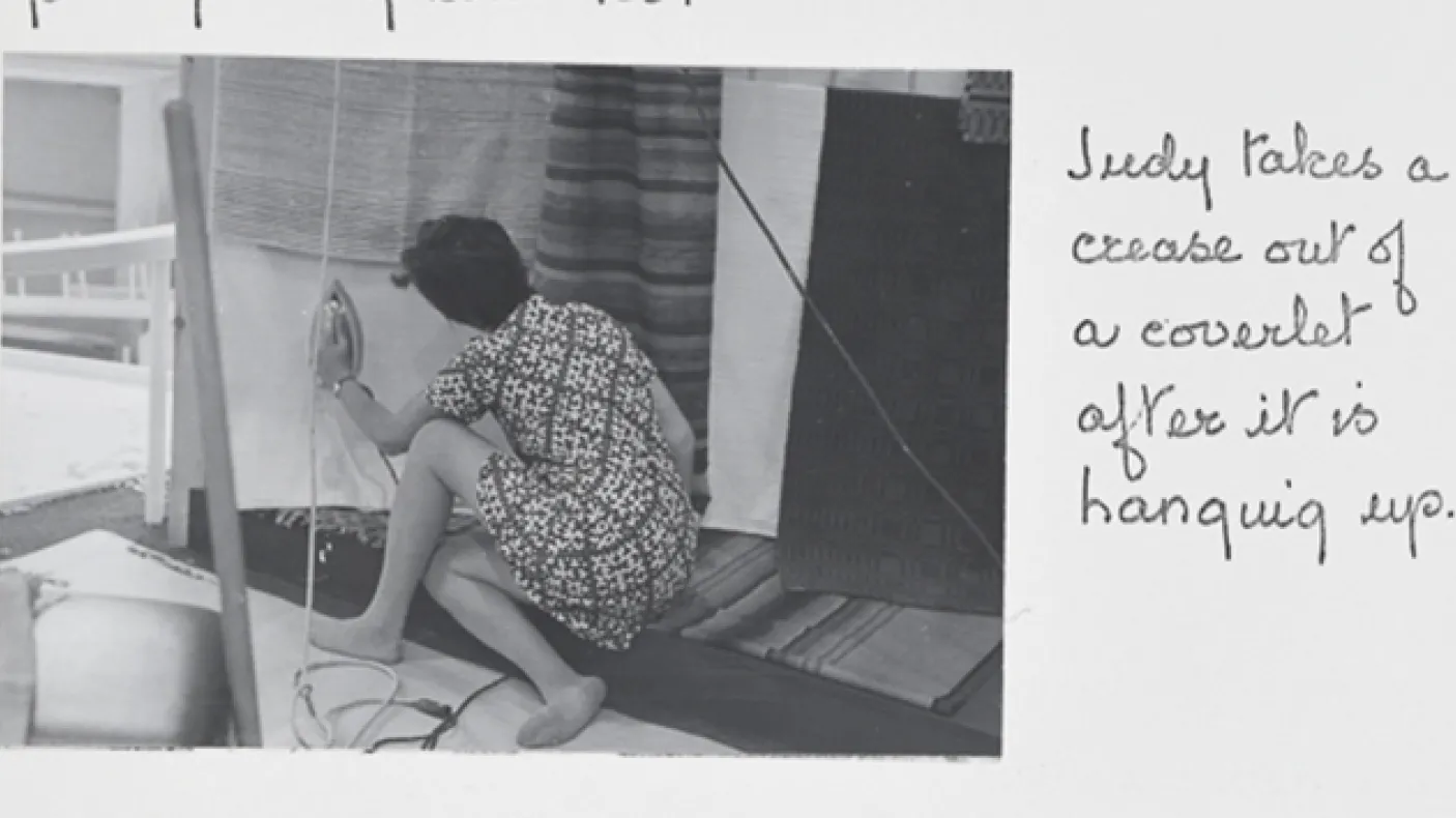 "Judy takes a crease out of a coverlet after it is hanging up."
