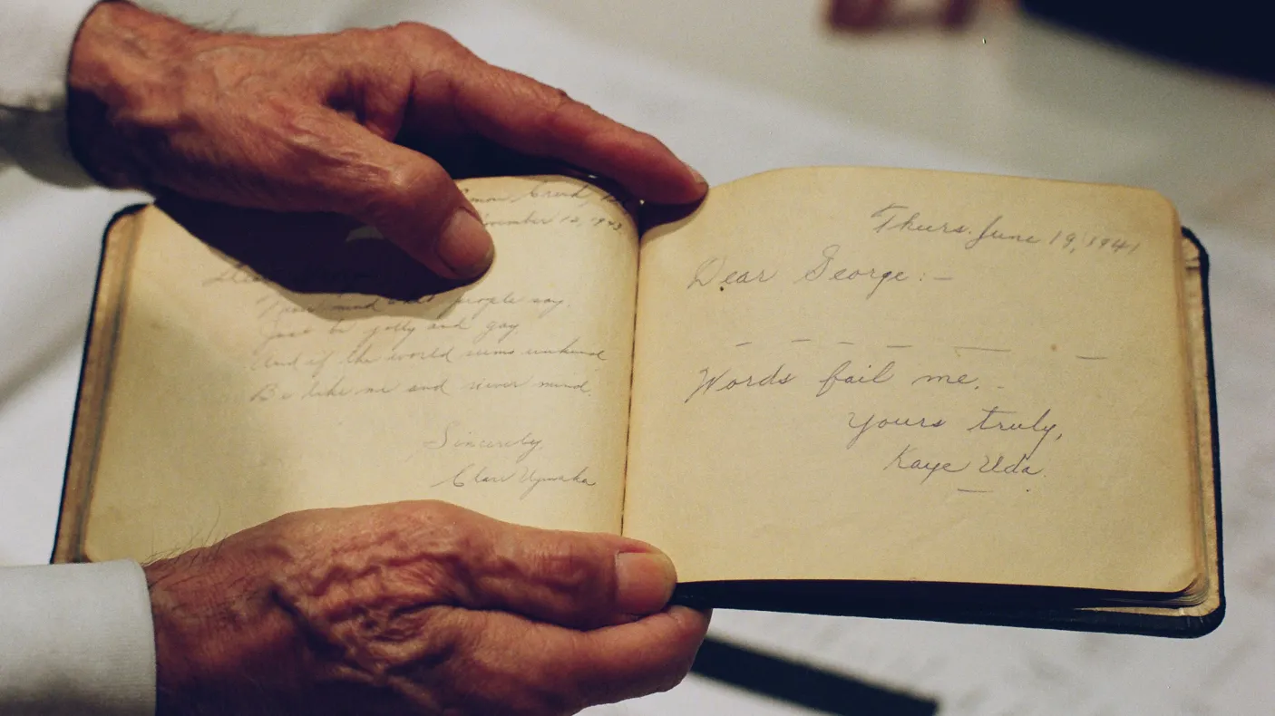Photo of a pair of hands holding a handwritten book. The entry reads: Dear George, Words fail me. Yours truly, Kaye Uda.
