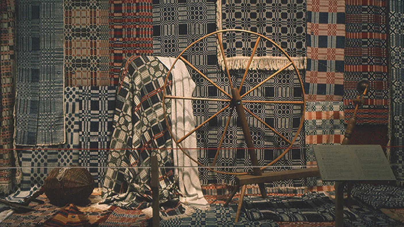 Photograph of textiles behind a spinning wheel
