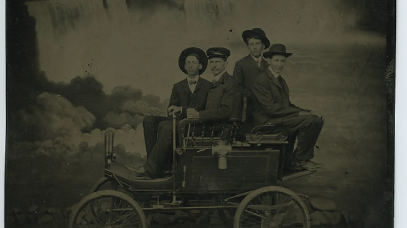 Photo de ferrotype noir et blanc de quatre hommes assis sur un chariot devant les chutes du Niagara
