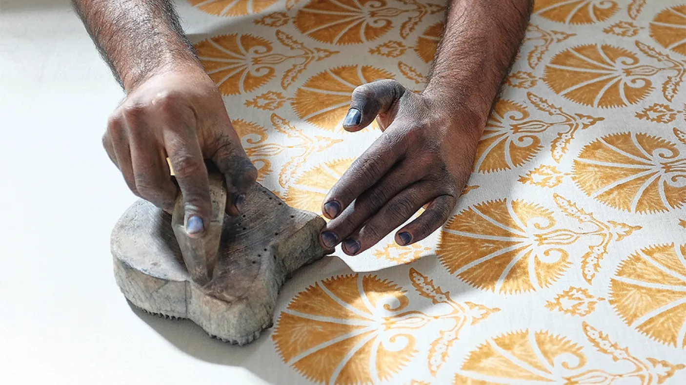 Hands pressing a stamp with yellow paint onto white fabric.