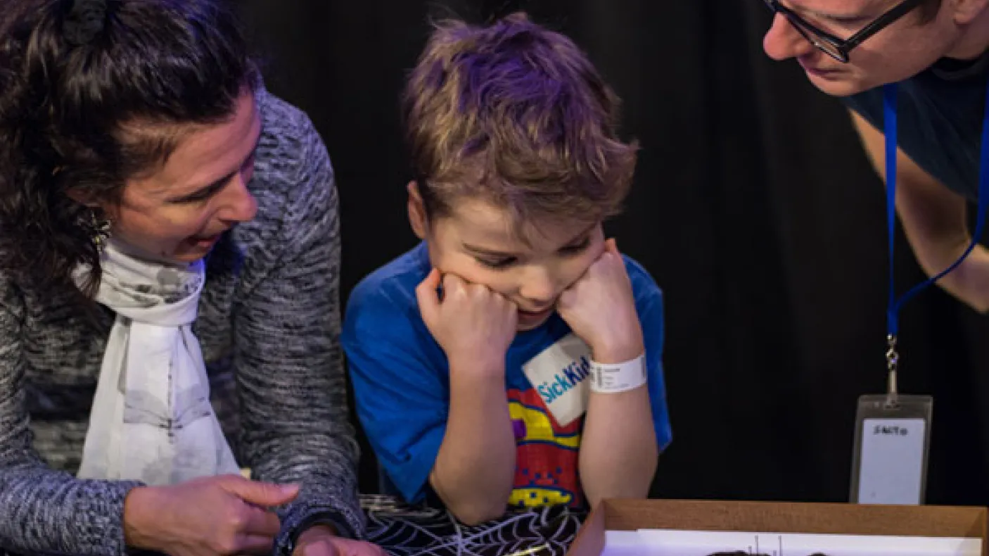 A child examines a spider specimen with adults

