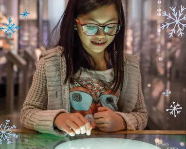 Une jeune fille regarde et sourit, émerveillée, alors qu'elle utilise un écran dans le Musée.