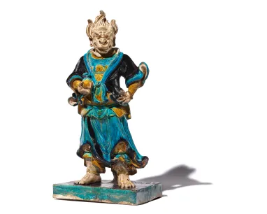 Statue of a ceramic underworld figure dressed in blue and green, on a white background