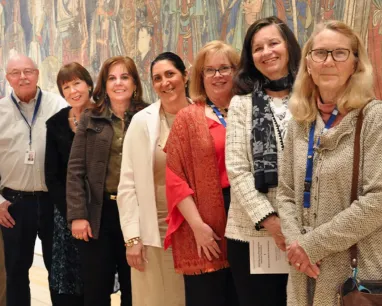 A diverse group of people poses in front of a colorful mural, showcasing their smiles and the vibrant artwork behind them.