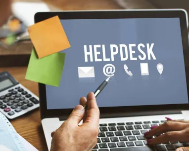 A man pointing at a laptop screen that says helpdesk with his pen with a person beside him.