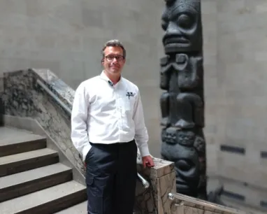 A man posing at the bottom of a stair case.