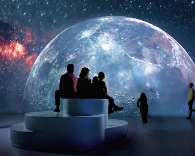 3 people sitting looking at a planet at the illuminarium