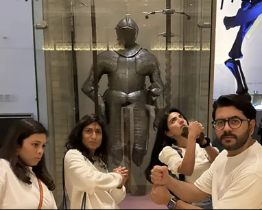 Four people posing in front of a knight's armor.