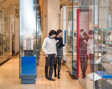 Deux visiteurs masqués regardent des objets exposés dans des vitrines à l'intérieur d'une galerie de musée.
