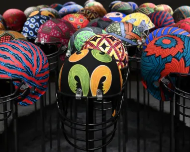 Un ensemble de casques colorés et à motifs, exposés sur des supports métalliques noirs, se détache sur un fond sombre.