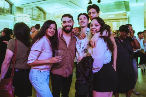 A group of people posing in a crowd with a green lighting in the background. A group of people posing in a crowd with a green lighting in the background.
