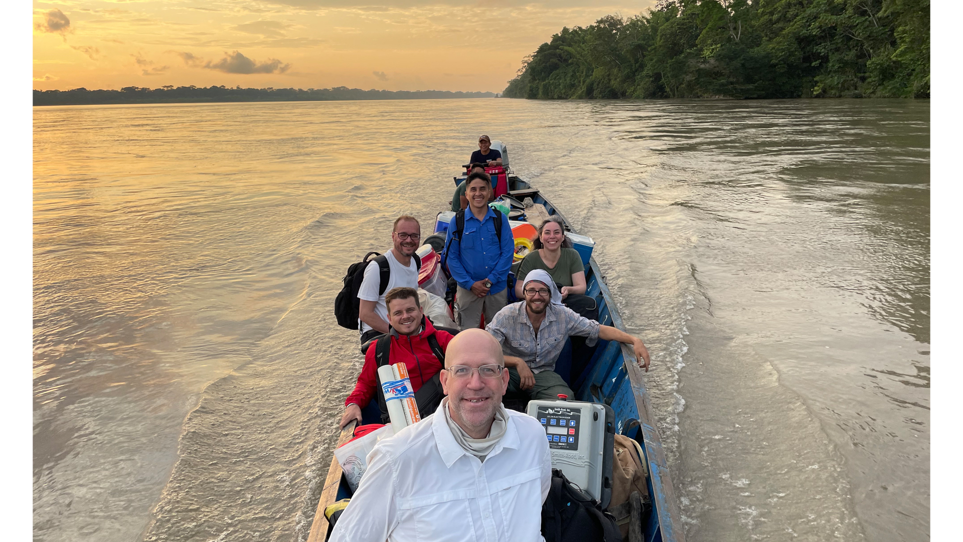 As the sun sets behind them, Dr. Nathan K. Lujan and his team boat down the Rio Napo, laden with an array of supplies. 