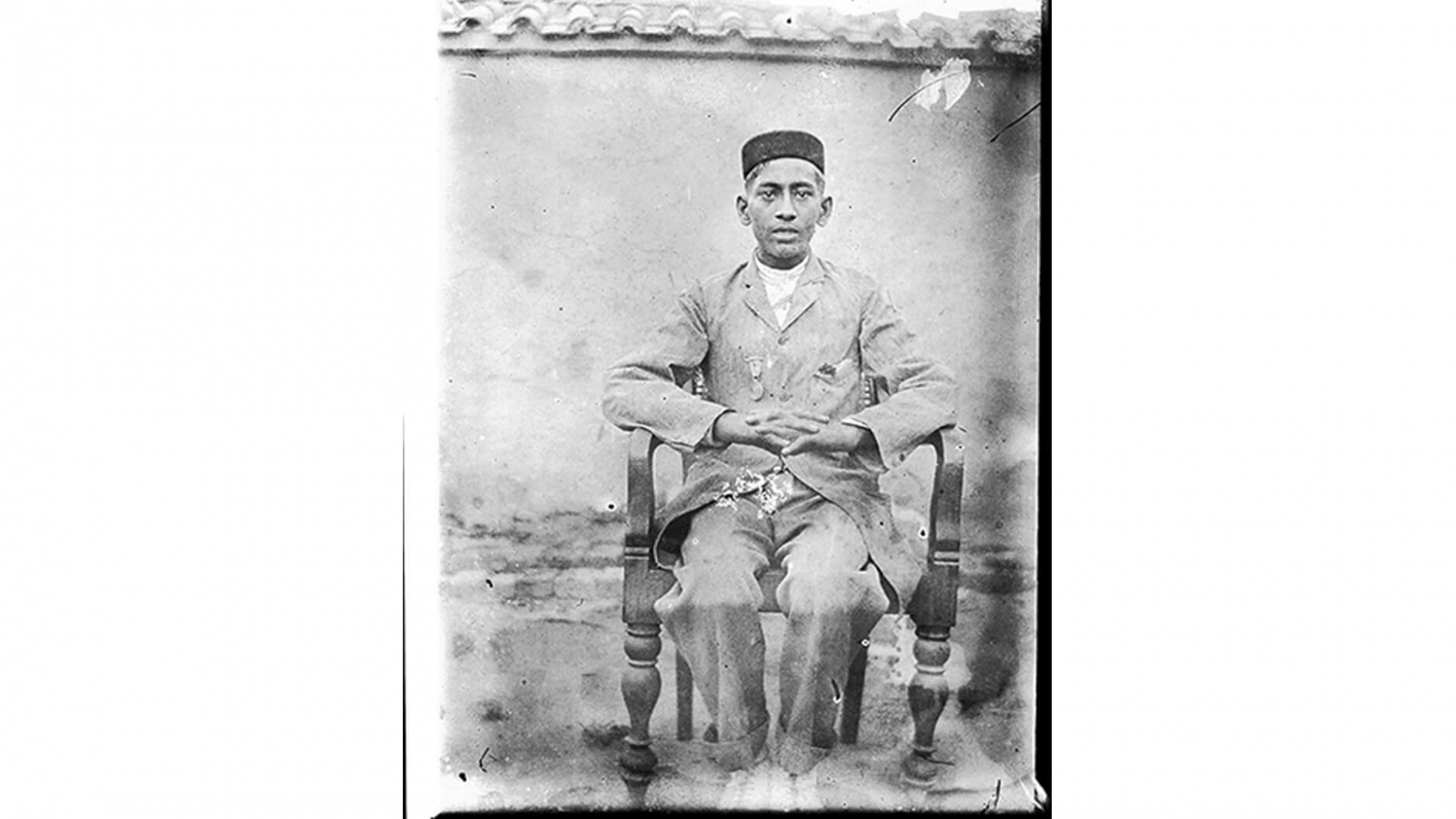 Seated portrait of a young man with a medal, silver gelatin glass plate negative.