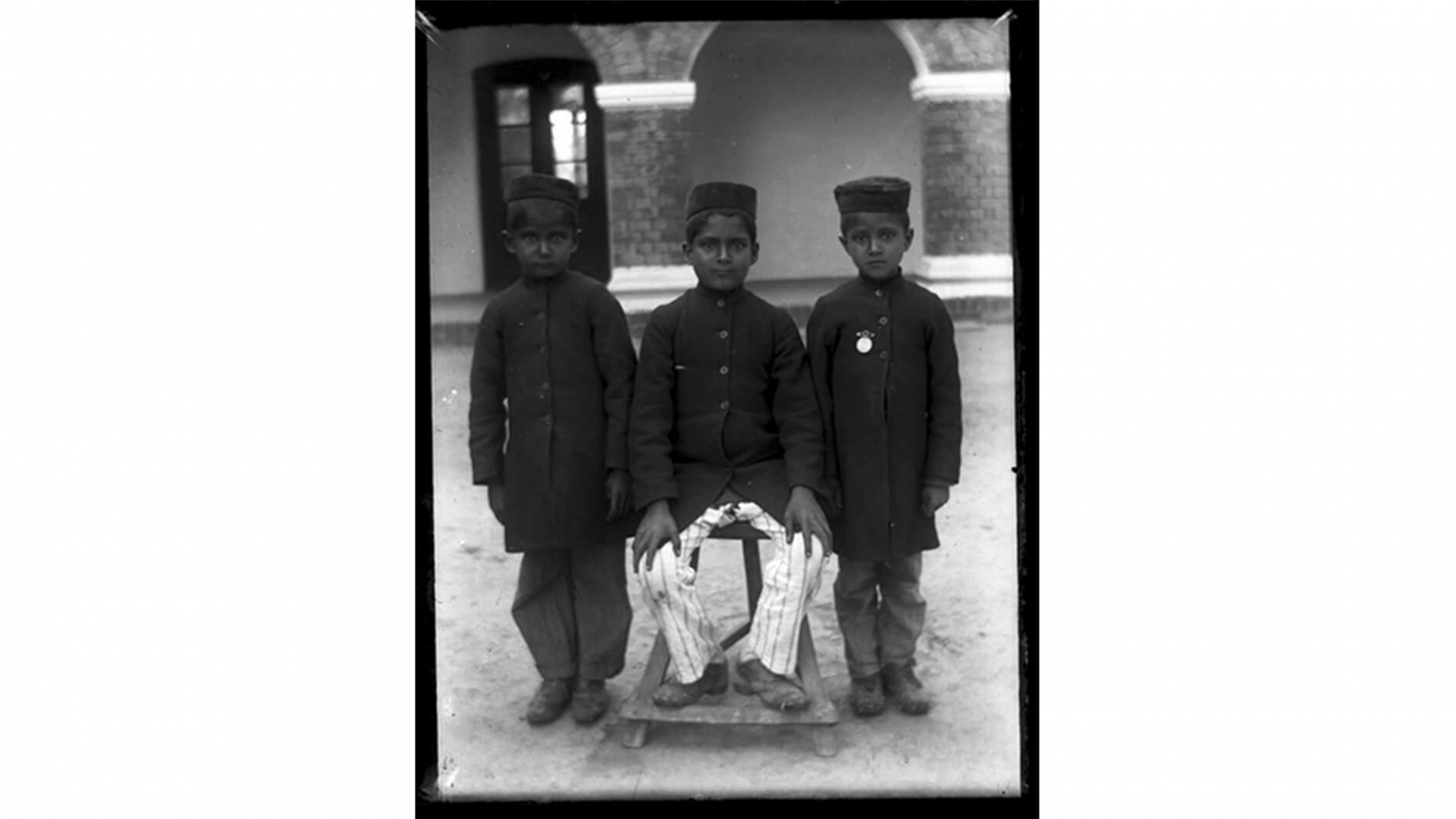 Portrait of three boys in dark jackets and hats, silver gelatin glass plate negative.