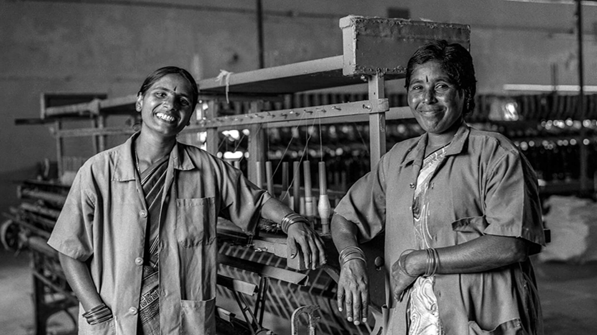 Two Indian craftspeople in front of textile manufacturing machine.
