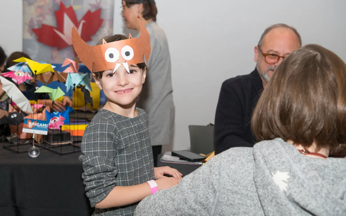 A girl smiles showing off the bat hat she has made with craft paper.