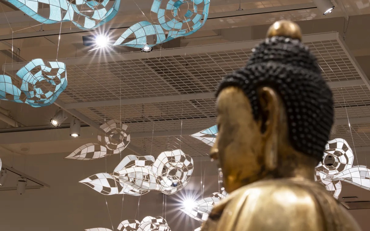 Paper clouds float in the sky above the head of a bronze buddah 