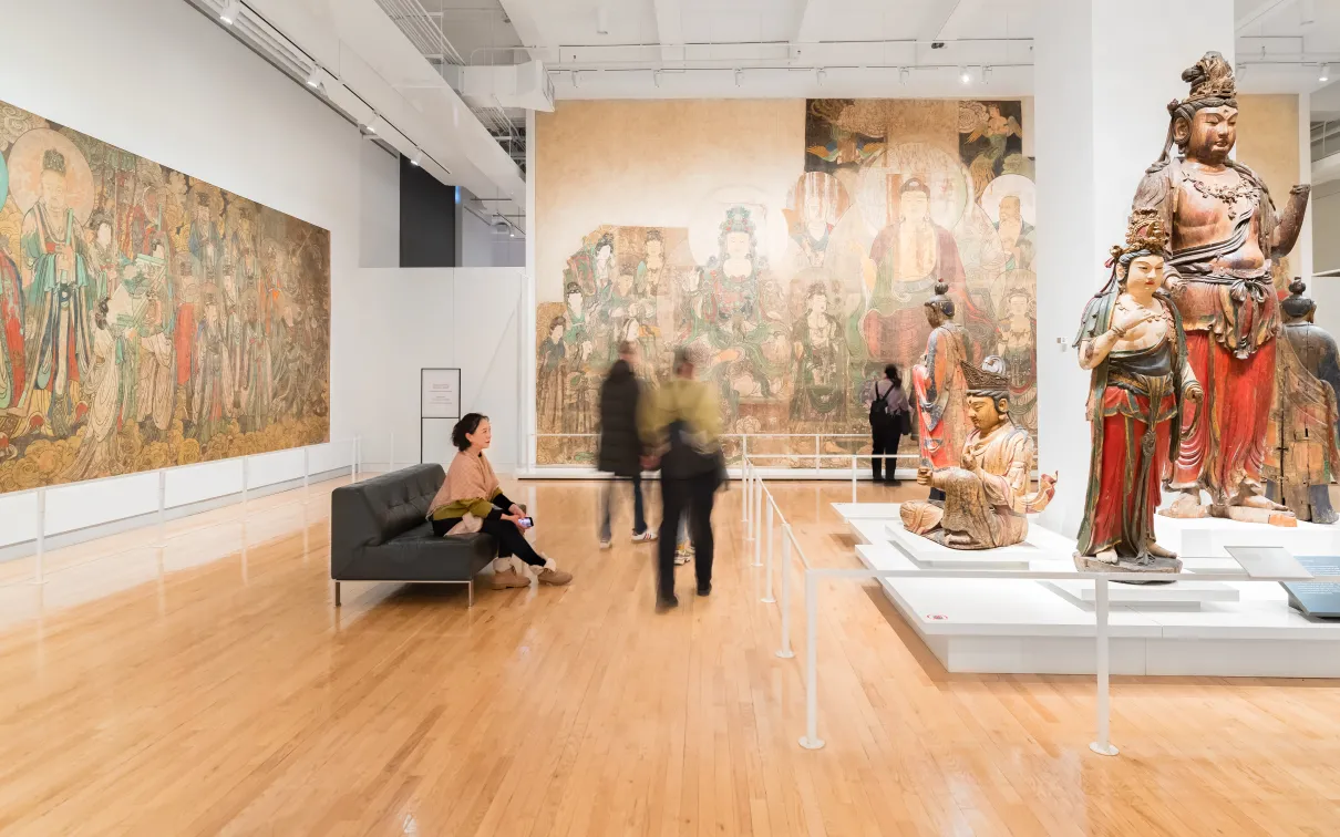 A woman sits still and enjoys a moment taking in ROMs Chinese temple art while other people move around her.