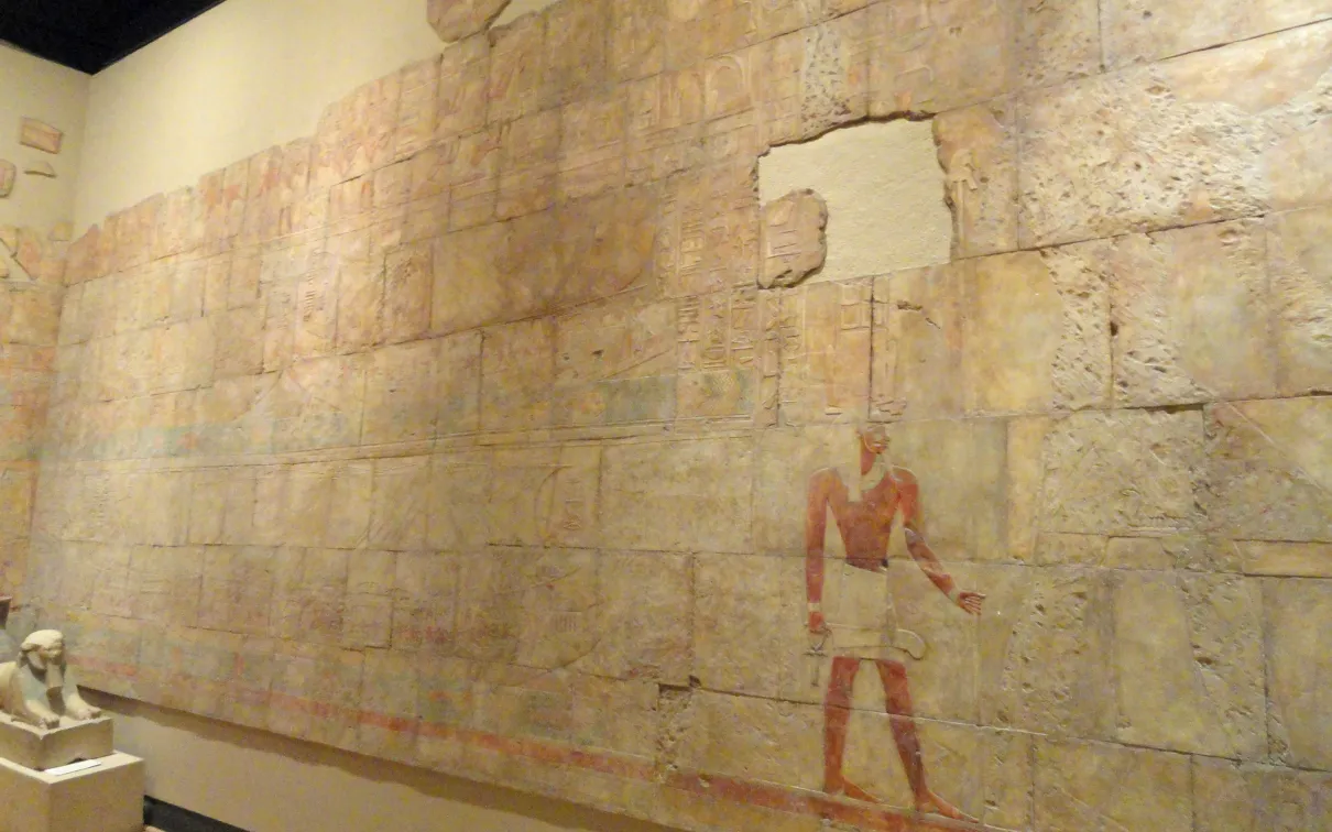 Mur d'un temple partiellement vandalisé représentant le voyage de la reine Hatchepsout à Pount. Un petit sphinx représentant le visage d'Hatchepsout se trouve dans le coin inférieur gauche.