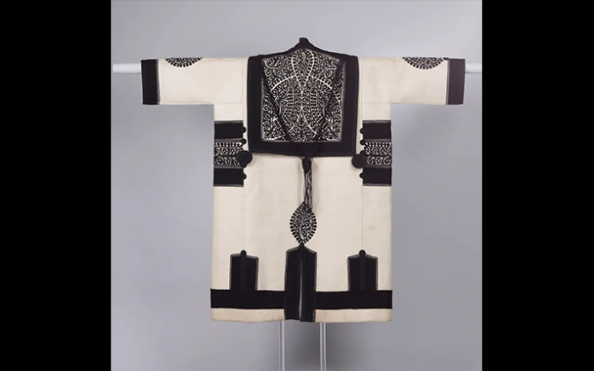 Szür (manteau) d'homme. Fabriqué dans l'actuelle Roumanie selon la tradition hongroise de Transylvanie. Vers 1900. Étoffe de laine blanche pleine, garnie de bandes appliquées de tissu noir et de motifs découpés en feutre noir ; garniture enrichie de petits ronds noirs noués. 970.227.9 Don de la Société hongroise Helikon, 1973.