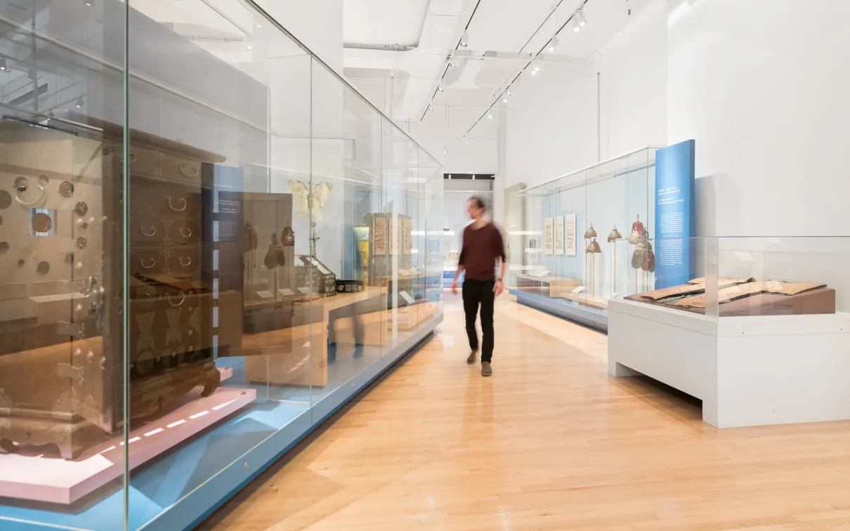 A person walks through a gallery admiring the large furniture in glass cases/
