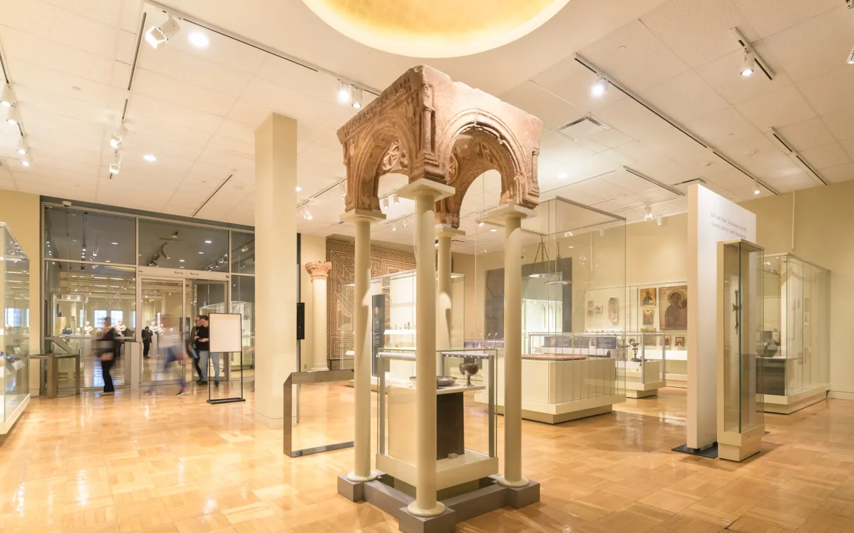 An ancient archway supported by modern pillars above a case containing a goblet and bowl.