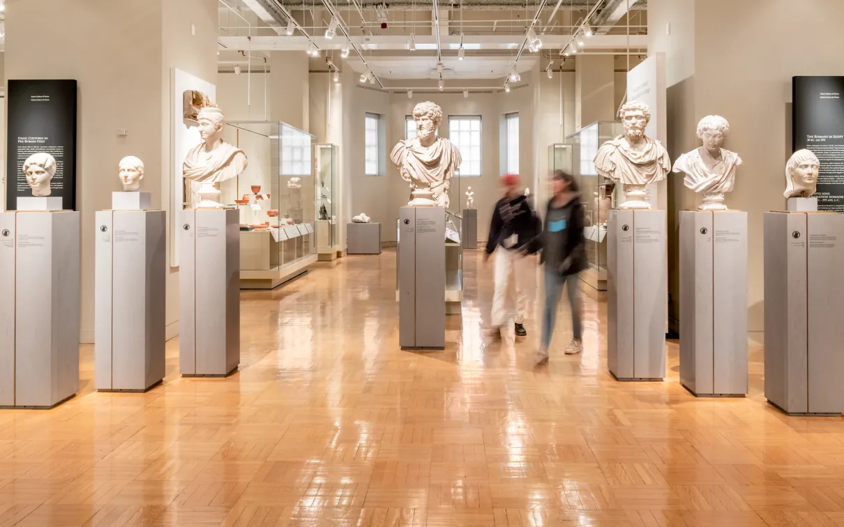 Two people walk among the marble busts of important Romans.