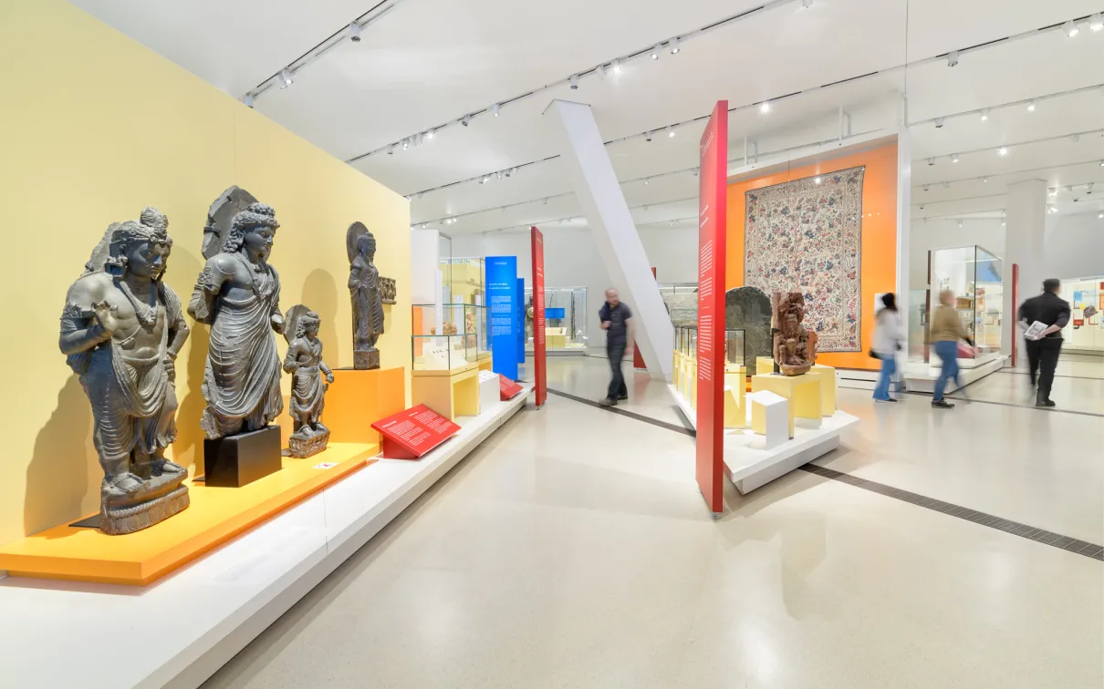 People walk around a gallery featuring statues of South Asian religious figures.