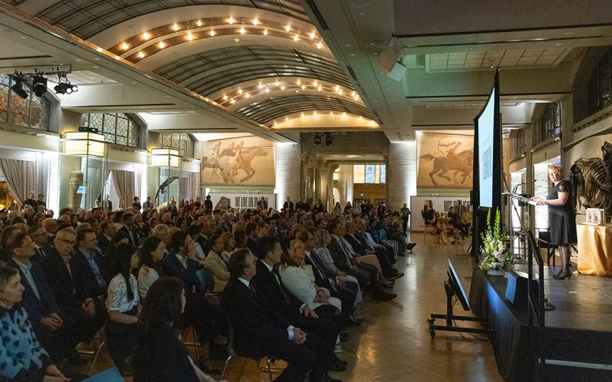Audience of people seated, listening to a speaker on stage