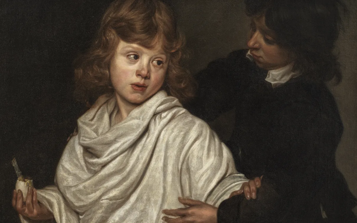 A young boy in a white shirt, holding a boiled egg, pushes another boy, in a black tunic, away from the egg.