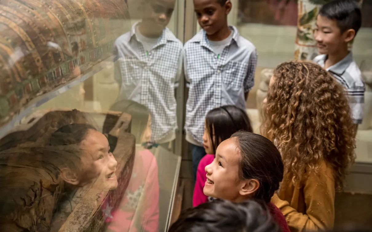 Children looking at an ancient Egyptian mummy display in a museum exhibit.