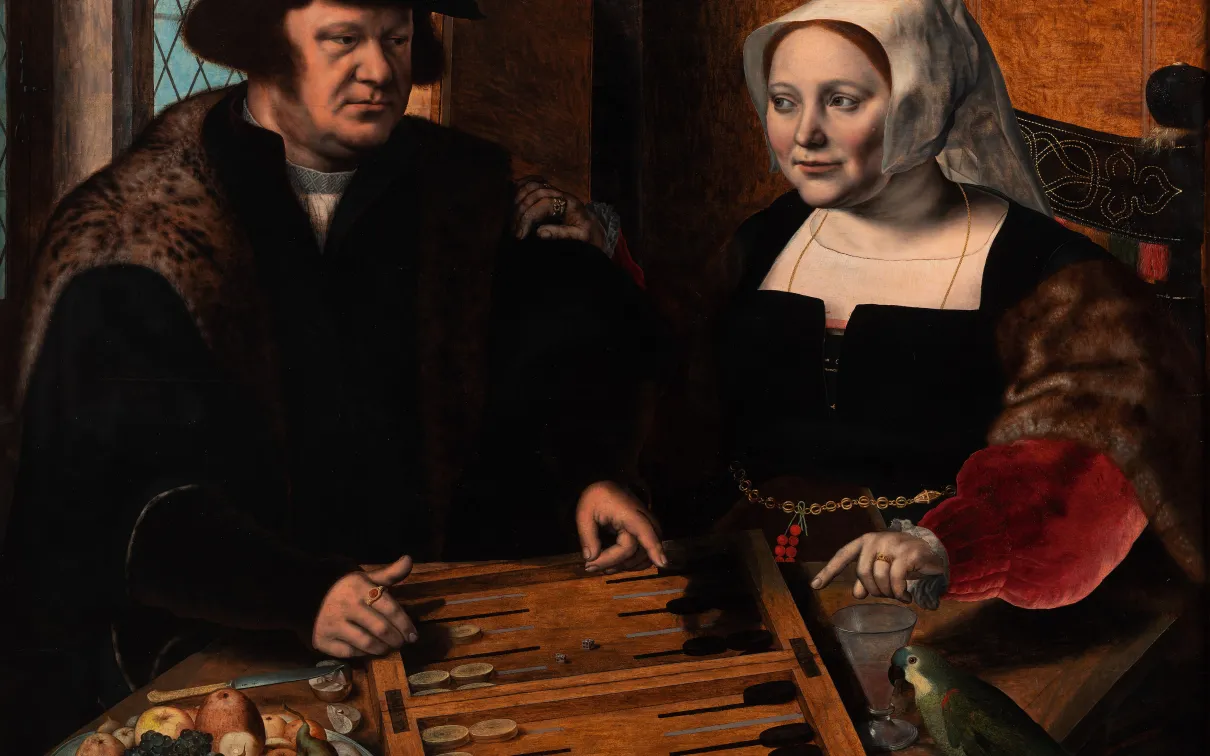 A well dressed couple sit at a table conversing and playing a board game.