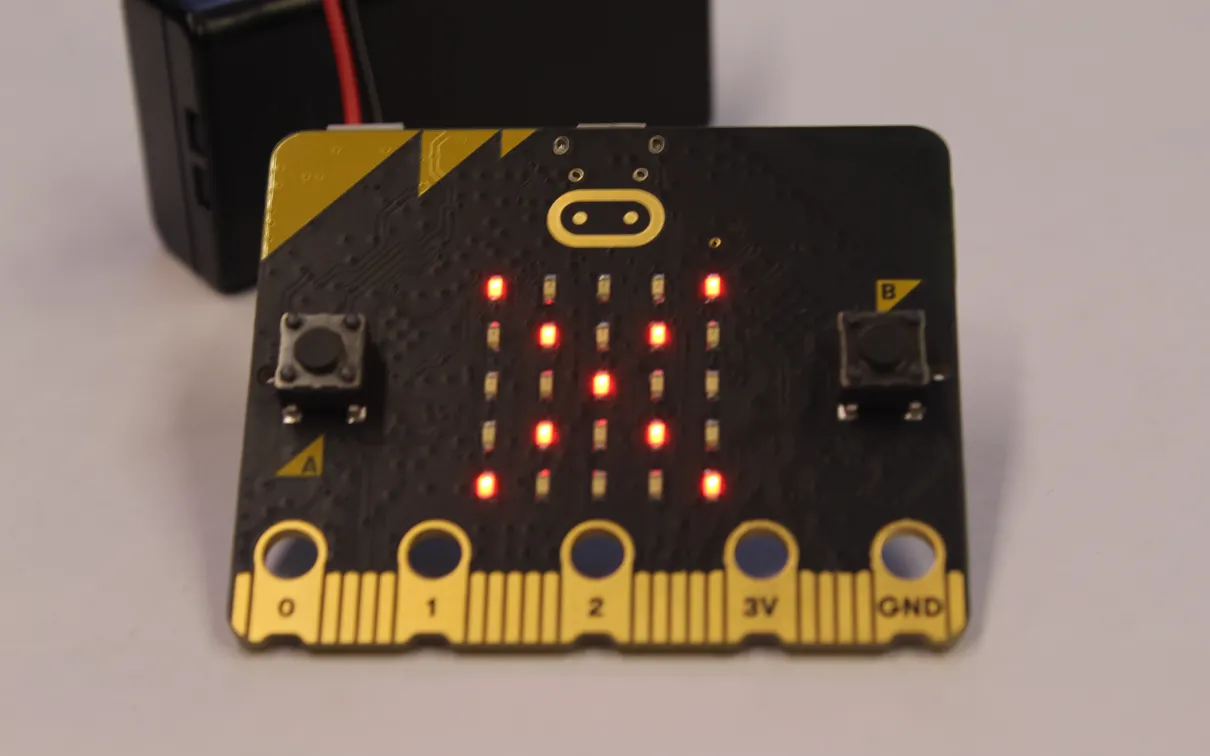 A black MicroBit displays illuminated LEDs in the form of an X