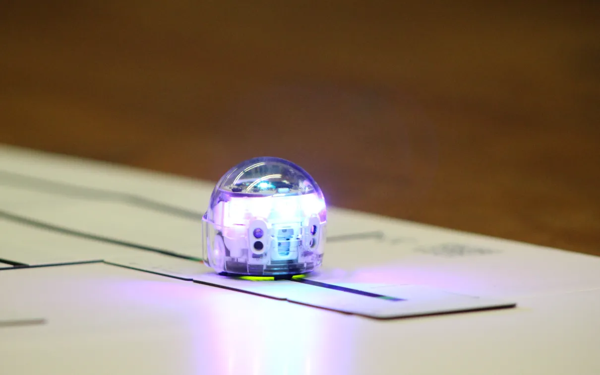 A small silver robot rolls along a dark track on a paper