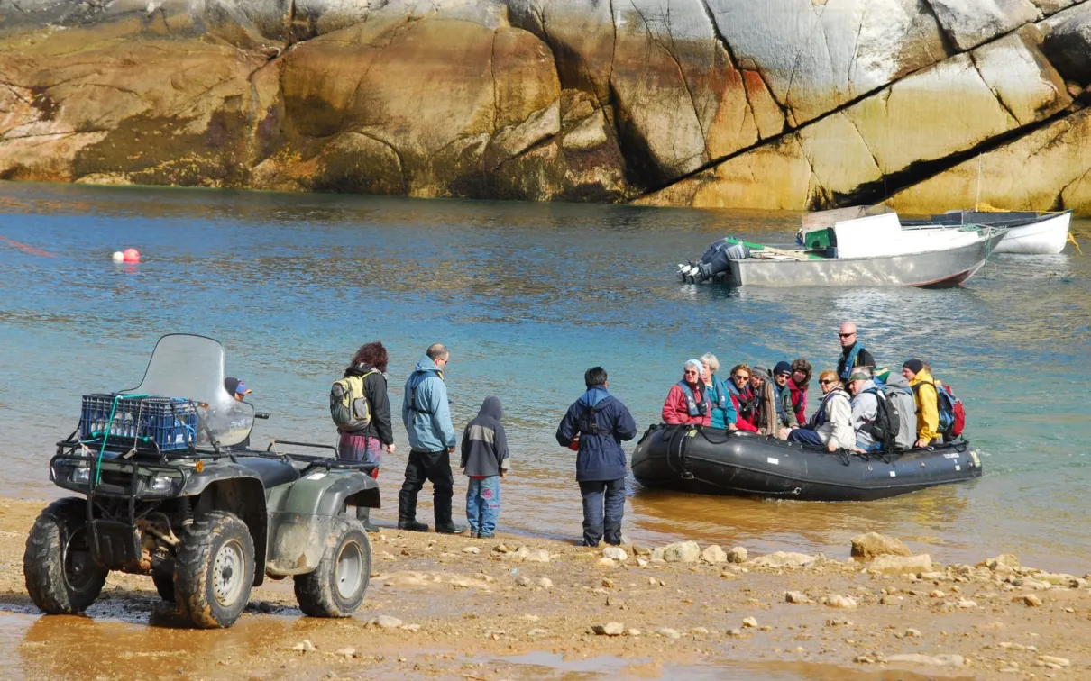 A group of people in a Zodiac boat arriving at shore.