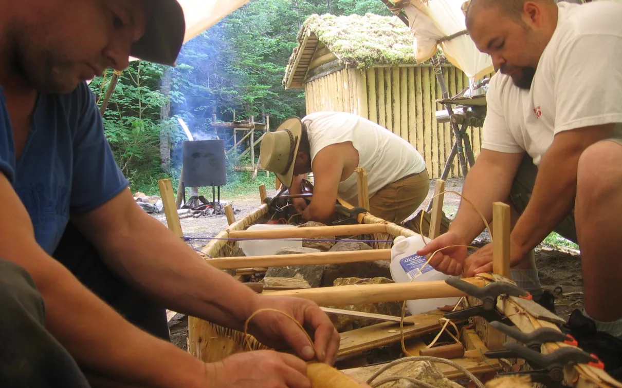 Three men making a birch bark canoe.