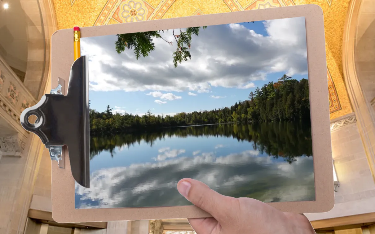 A hand holds a clipboard in front of a gallery at ROM. The clipboard displays an image of a glassy lake ringed by trees